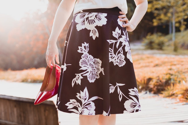 Žena v čiernej sukni s bielymi vzormi drží v rukách topánky.jpg